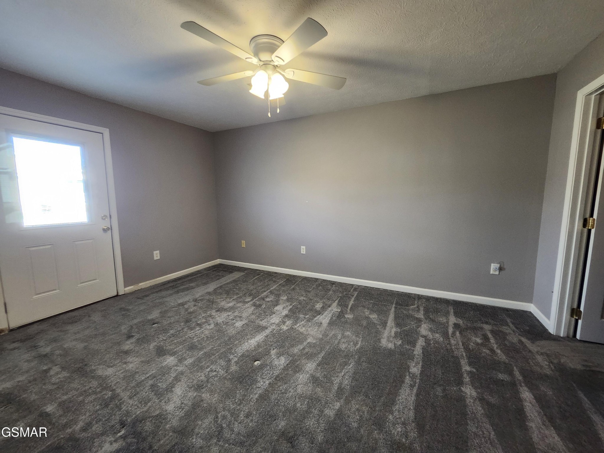Empty carpeted room with gray walls, a ceiling fan, and a windowed exterior door.
