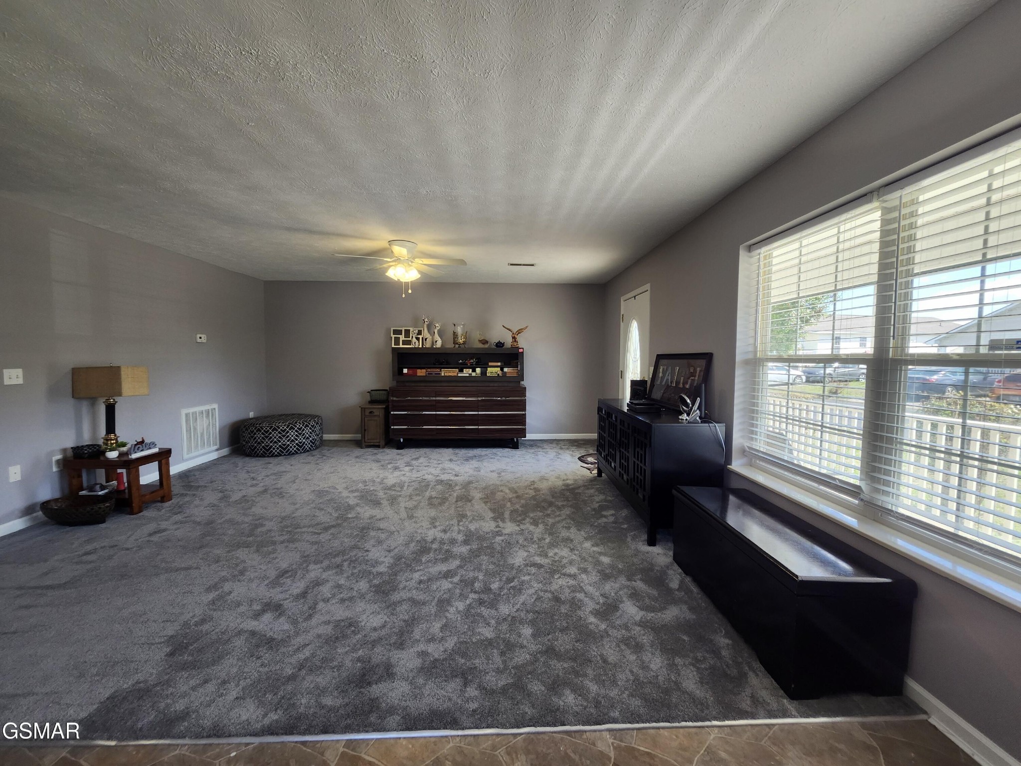 Furnished living room with gray carpet, dark wood cabinets, and large windows with blinds.