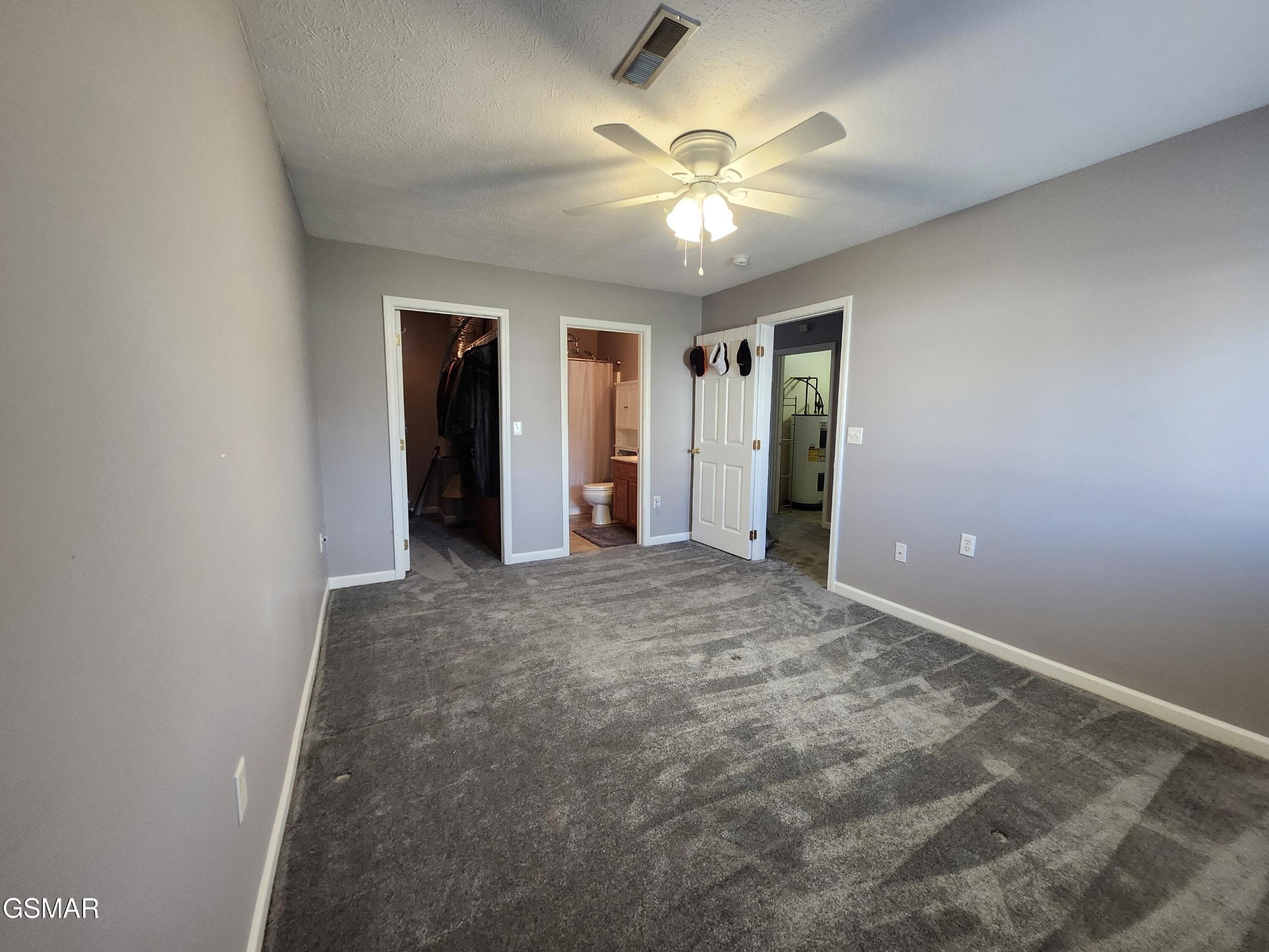 Unfurnished bedroom with gray carpet, ceiling fan, and doorways to a closet and bathroom.