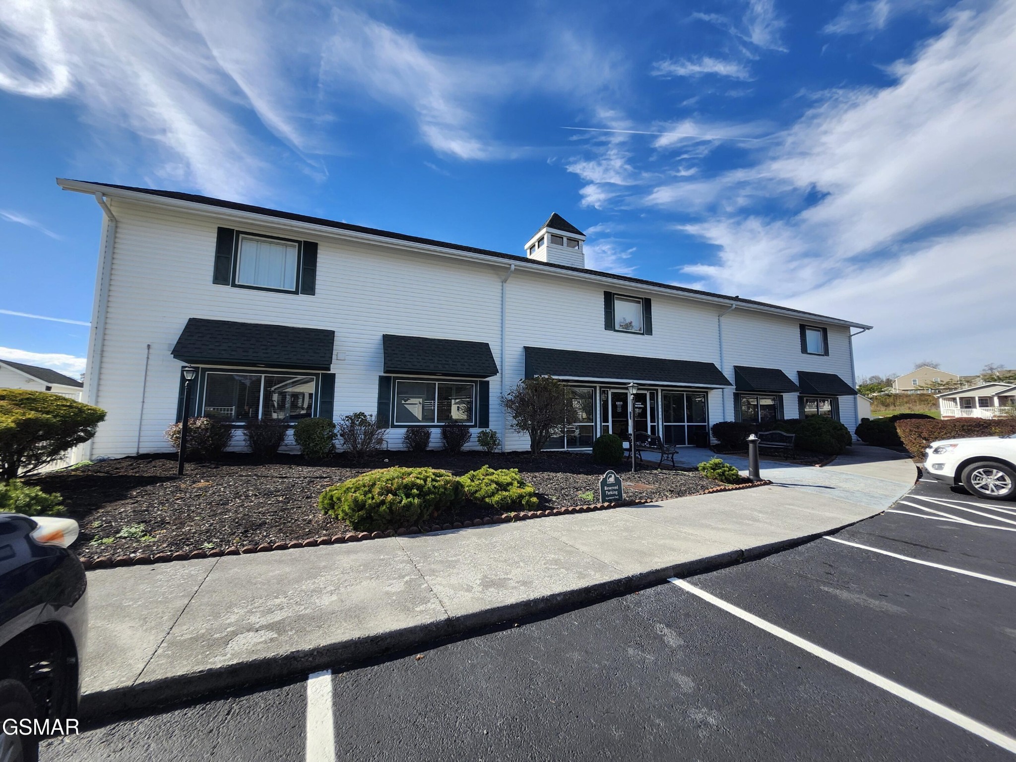 White two-story building with black window awnings, landscaped frontage, and a parking lot.