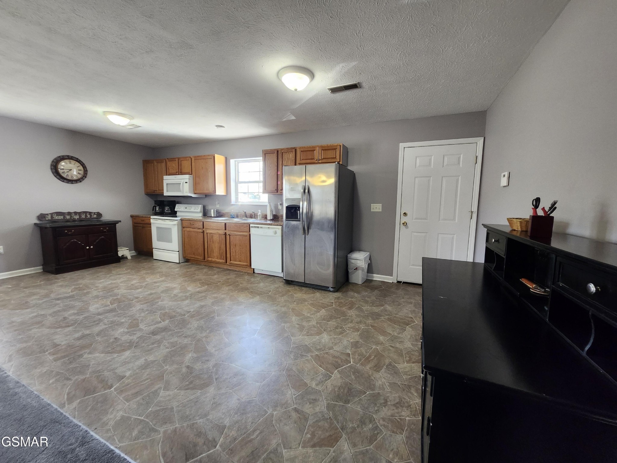 Kitchen with wood cabinets, stainless steel refrigerator, white appliances, and patterned tile flooring.