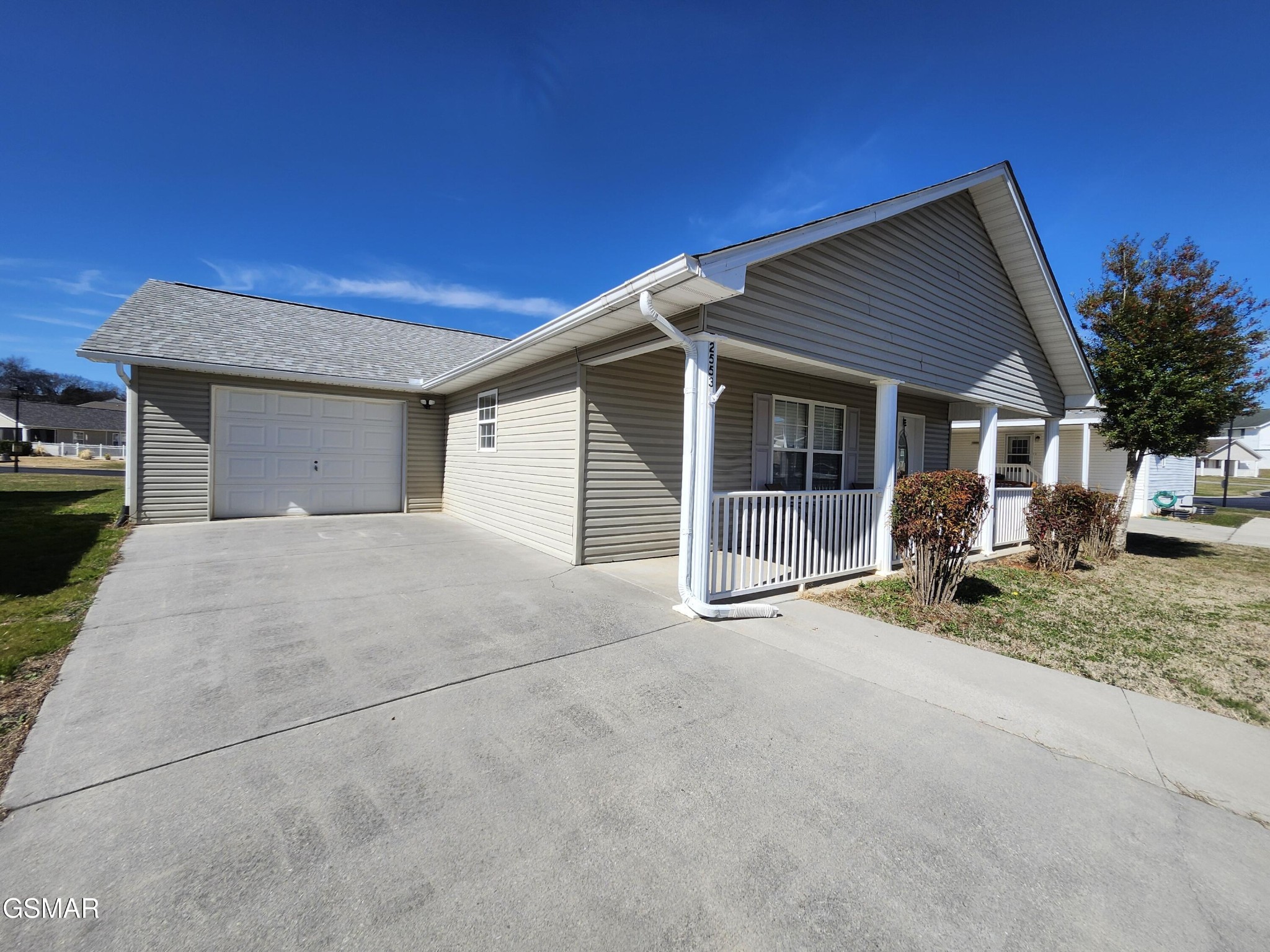 Gray-sided home with a white garage door, covered porch, and wide concrete driveway.