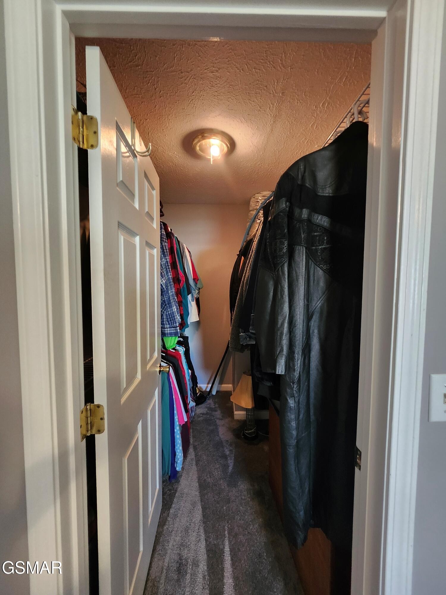 Walk-in closet with hanging clothes on both sides and gray carpet.