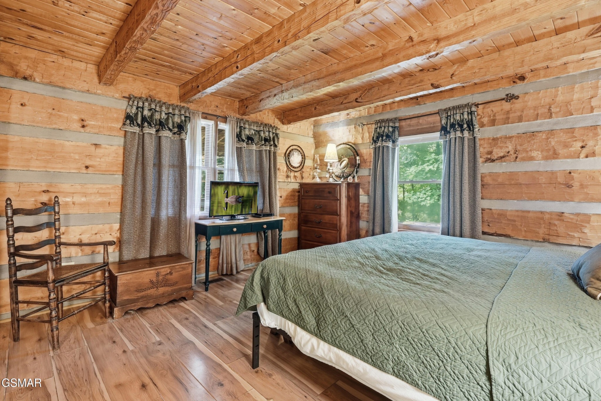 Rustic log cabin bedroom with a green-quilted bed, exposed timber beams, and a wooden rocking chair.