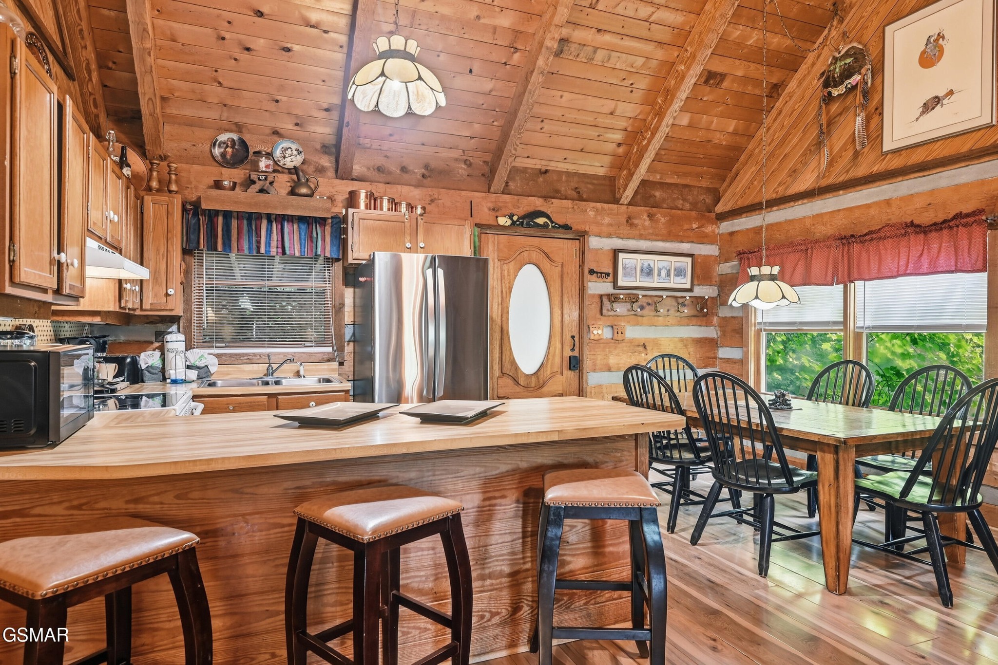 Rustic wood kitchen and dining area with a large island, bar stools, and windows overlooking greenery.