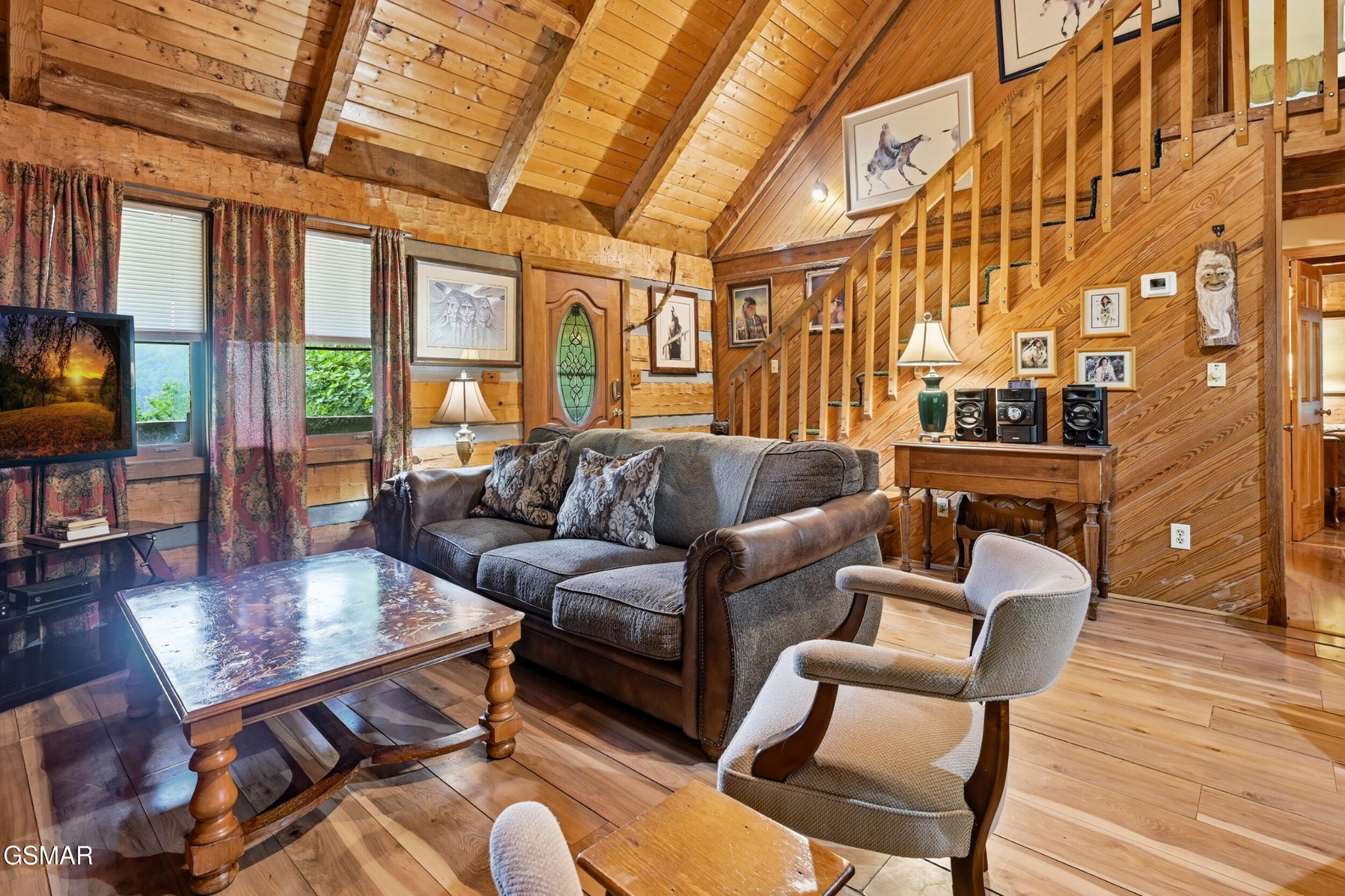 Wood-paneled living room with a vaulted ceiling, staircase, and gray sofa.