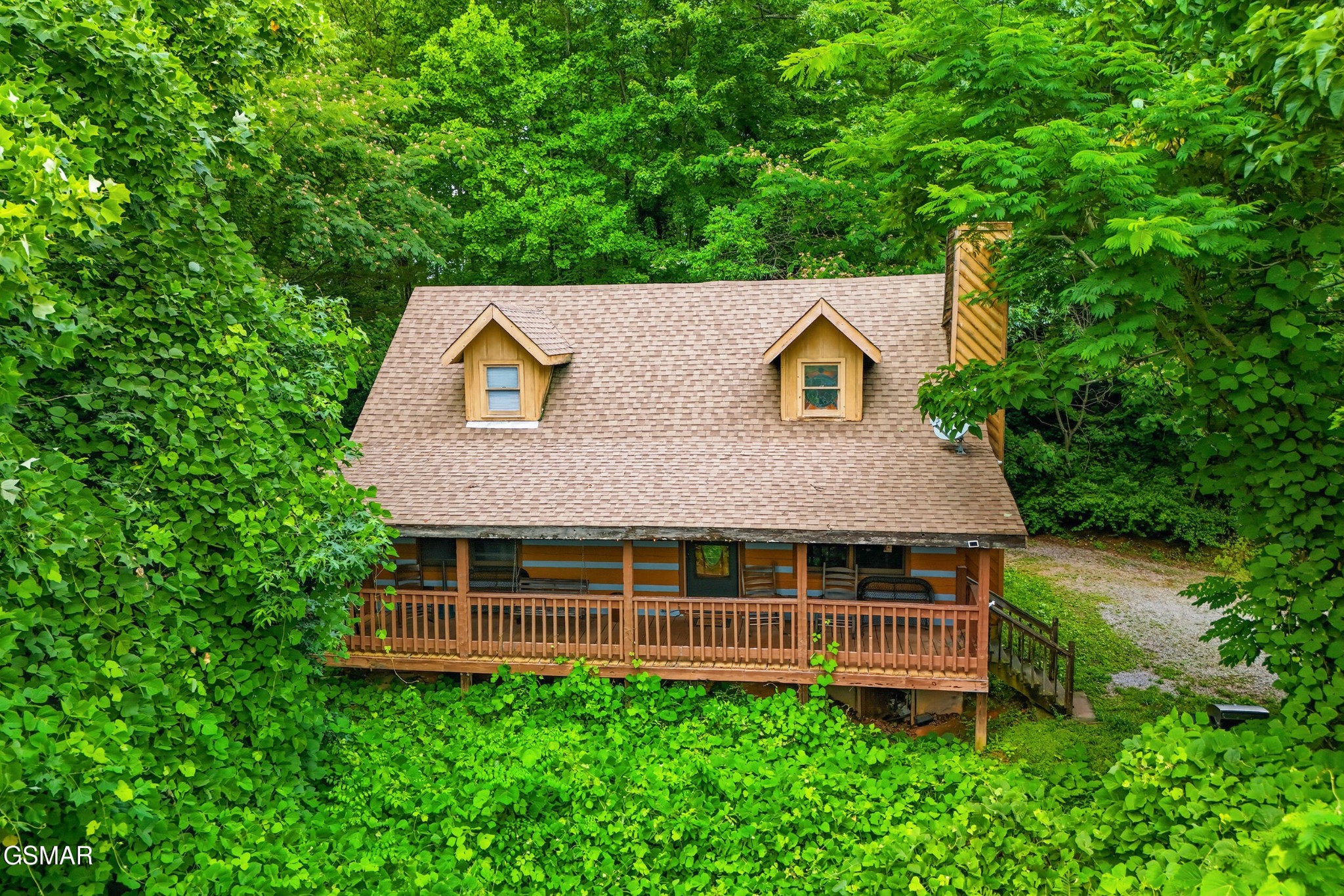 Wooden cabin with a covered porch surrounded by dense green woodland.