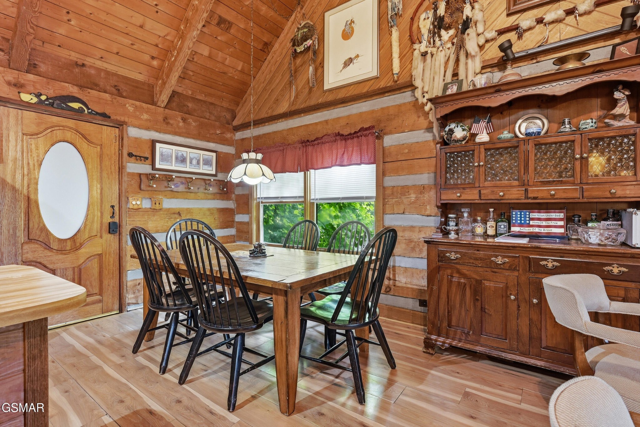 Log cabin dining room with a wooden table, vaulted timber ceiling, and large china cabinet.
