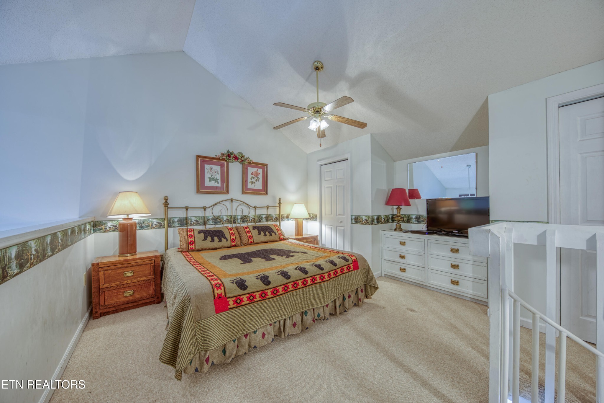 Furnished bedroom with a bear-patterned bedspread, wood nightstand, dresser, and television.