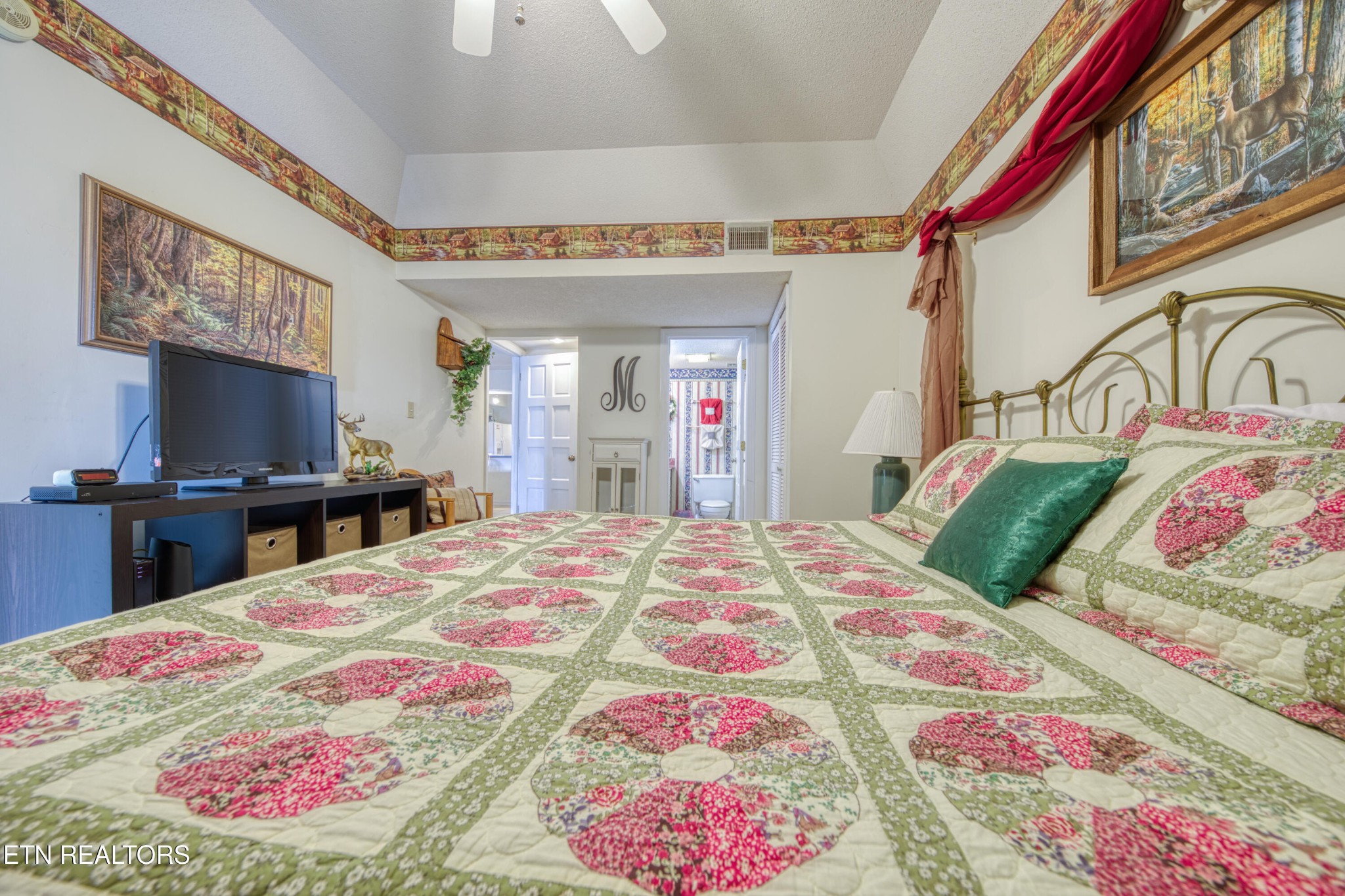 Bedroom with a floral quilt, brass bed, and television on a media console.