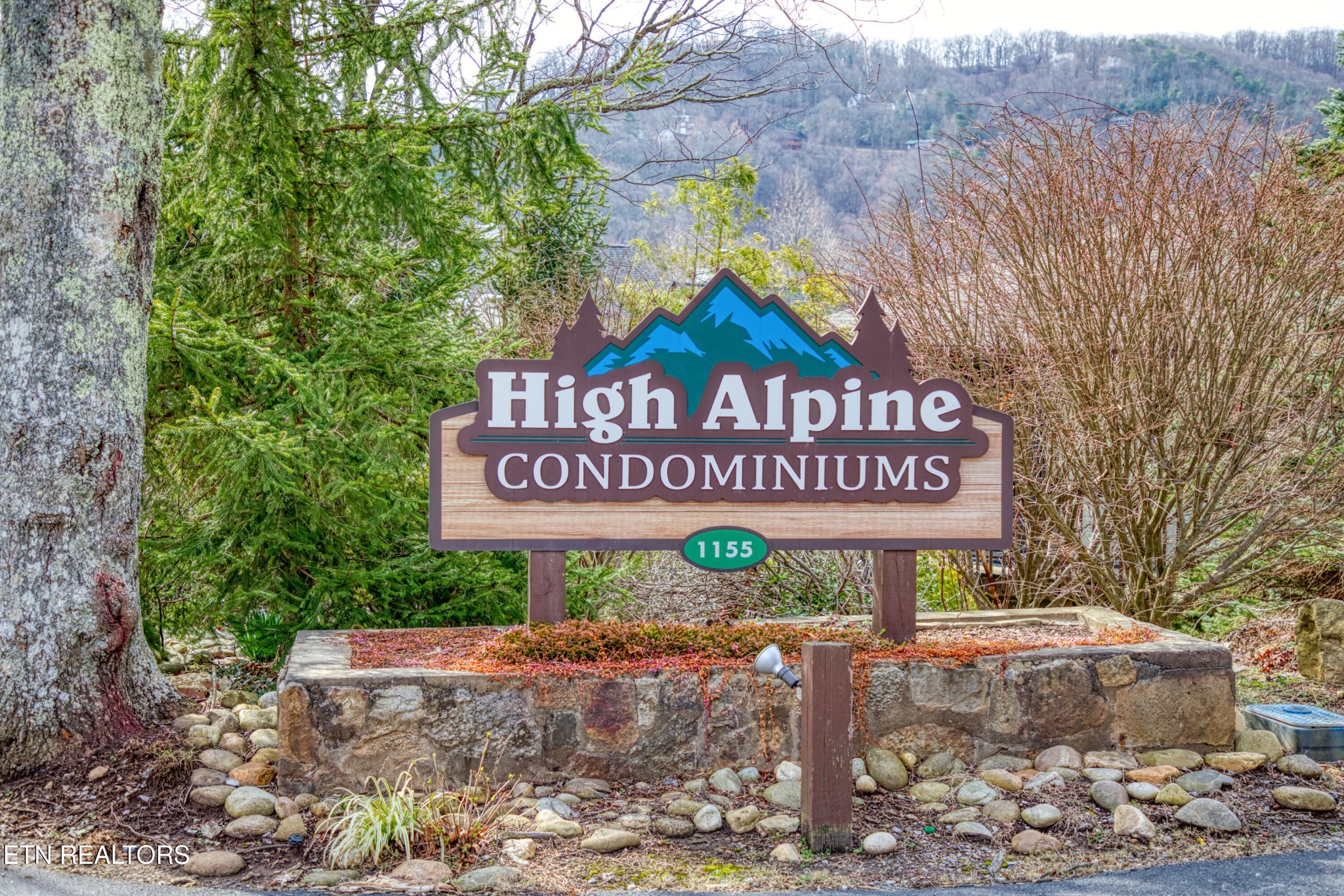High Alpine Condominiums entrance sign marked 1155, surrounded by trees and stone landscaping.