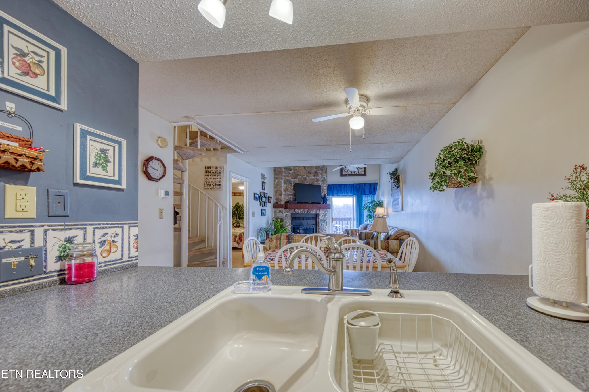 Kitchen sink and countertop overlooking a dining area, curved staircase, and stone fireplace.