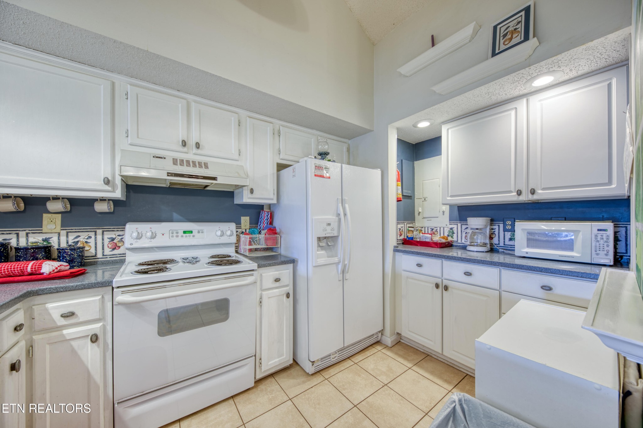 Kitchen with white cabinets, blue backsplash, white appliances, and decorative tile trim.