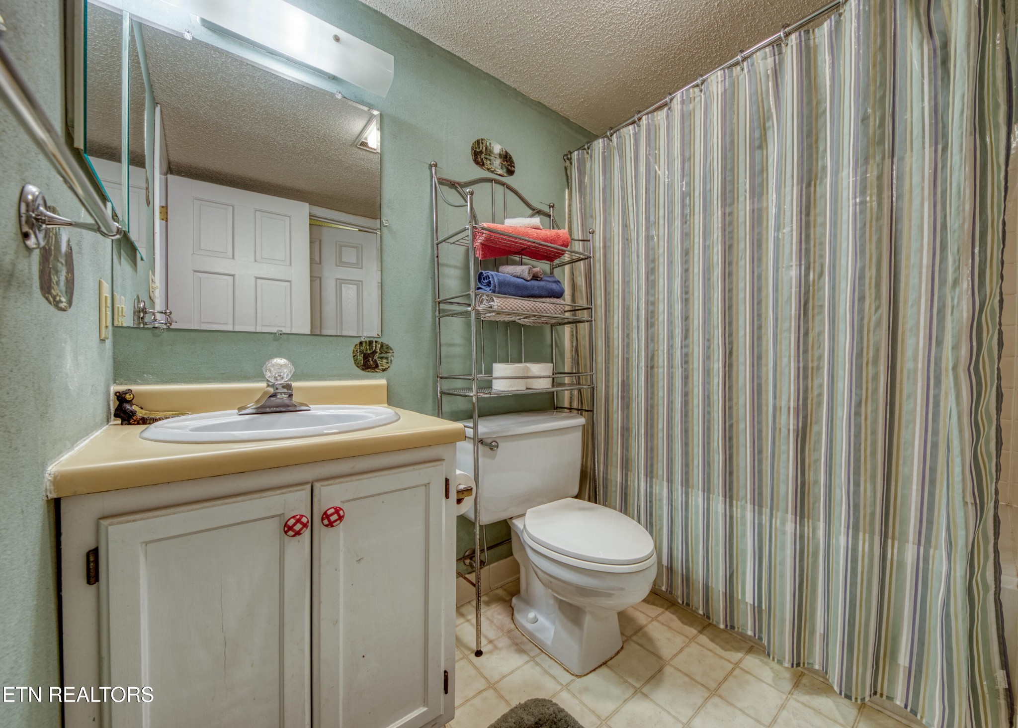 Bathroom with cream vanity, toilet, and striped shower curtain.