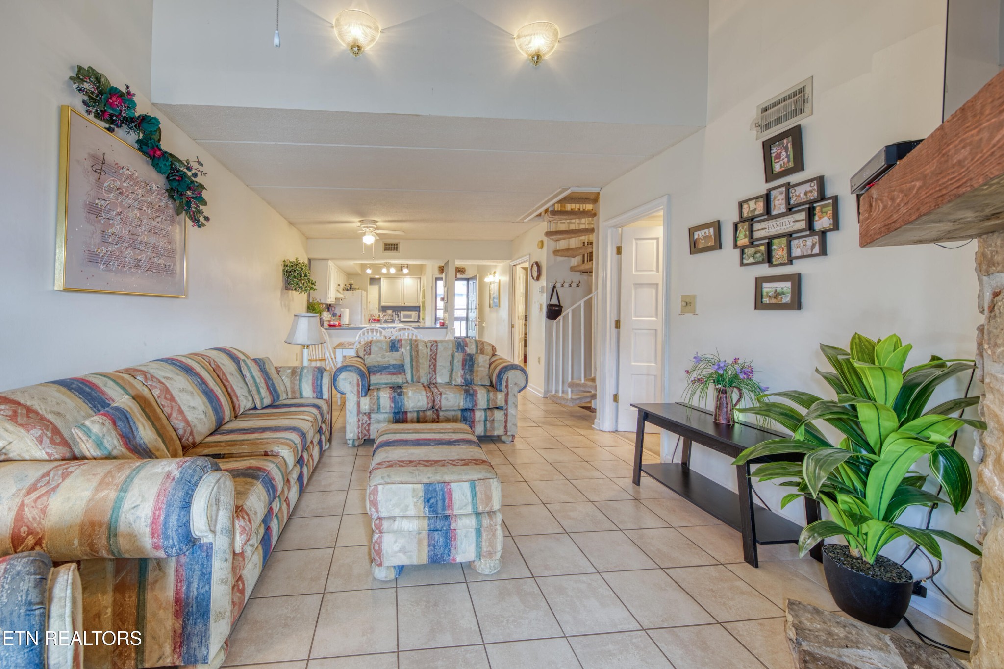Living room with colorful striped sofas, tiled floors, a staircase, and potted plants.