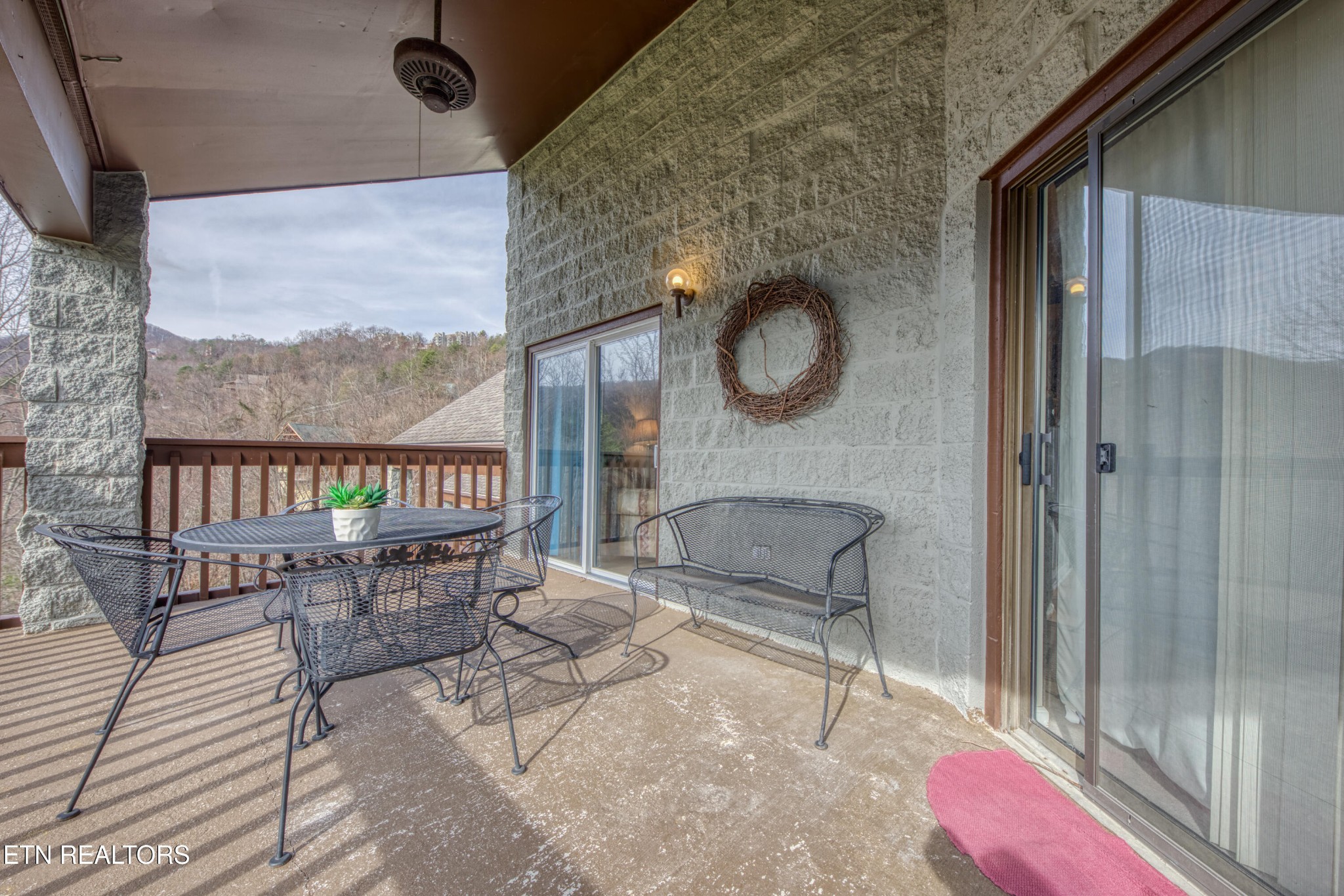 Covered condo balcony with metal patio furniture and a wooded mountain view.