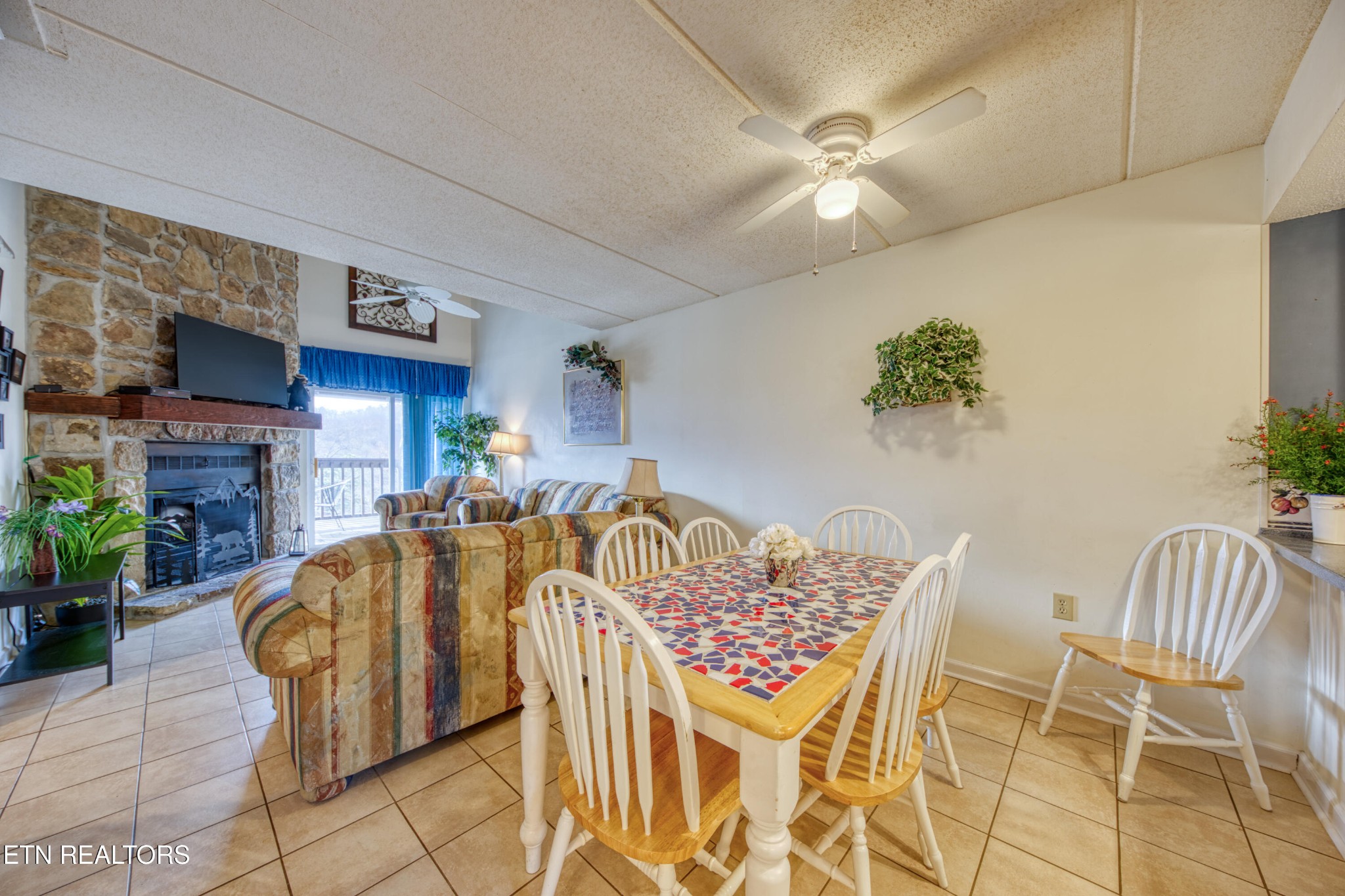 Living and dining area with a stone fireplace, striped sofas, and a white dining set.