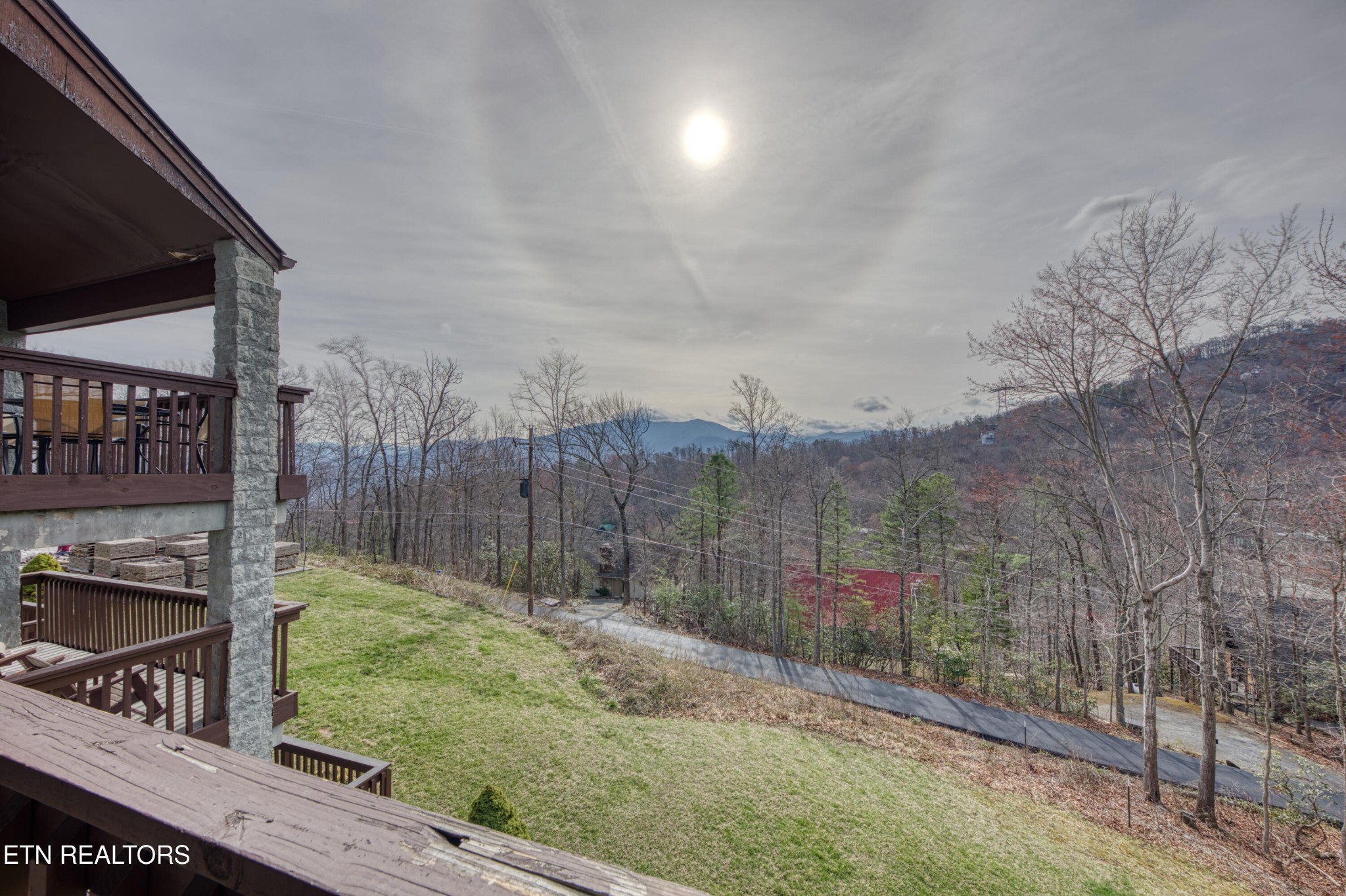 Wooden deck and lawn overlooking wooded hills and distant mountains beneath a cloudy sky.