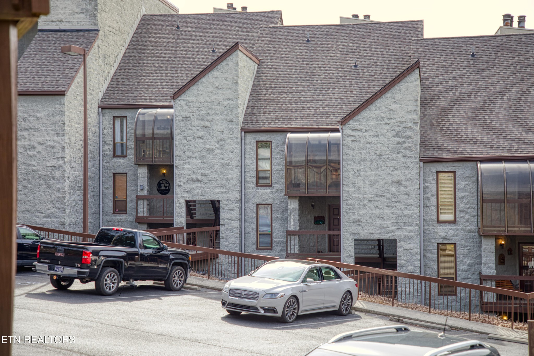 Gray stone townhouses with steep roofs, enclosed balconies, and cars parked along the front.