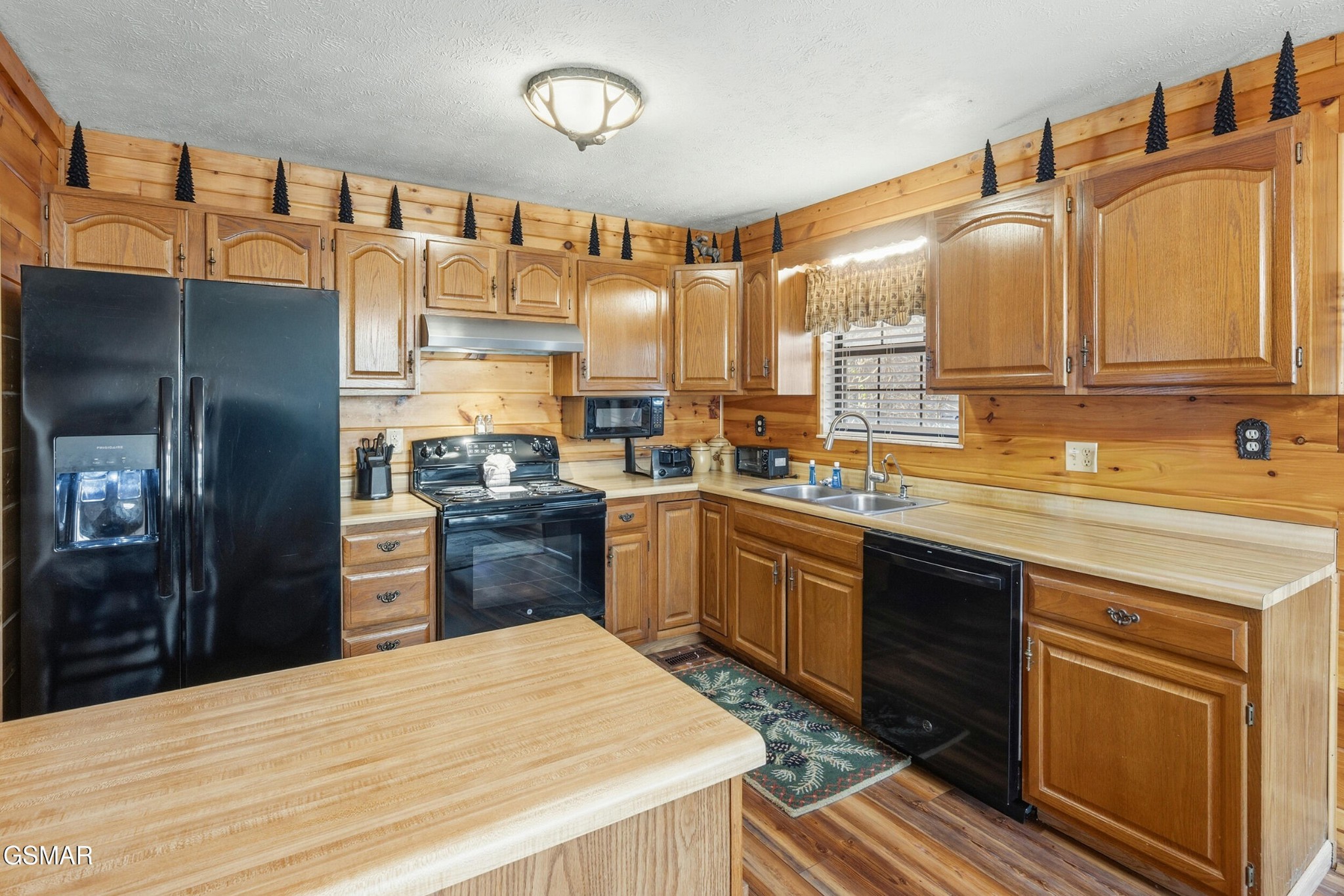 Rustic wood-paneled kitchen with black appliances, double sink, and a large wood-topped island.