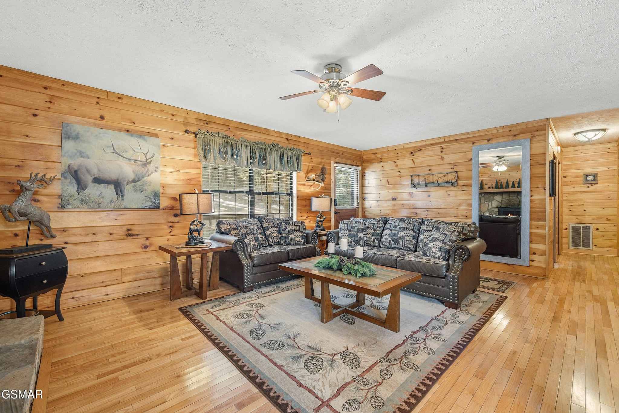 Wood-paneled living room with patterned sofas, hardwood floors, and deer-themed decor.