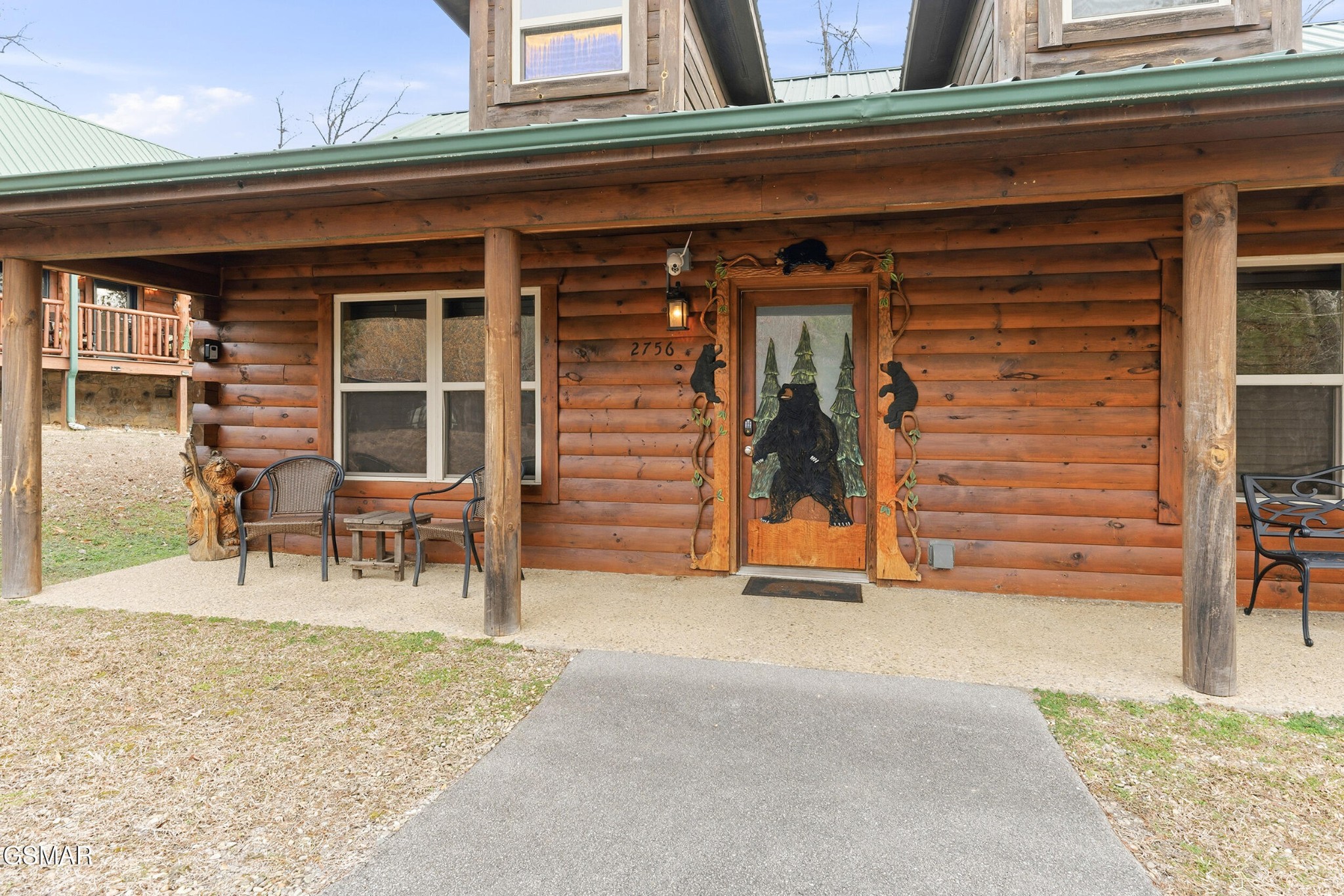 Log cabin entrance with a covered porch, green metal roof, and bear-decorated front door.