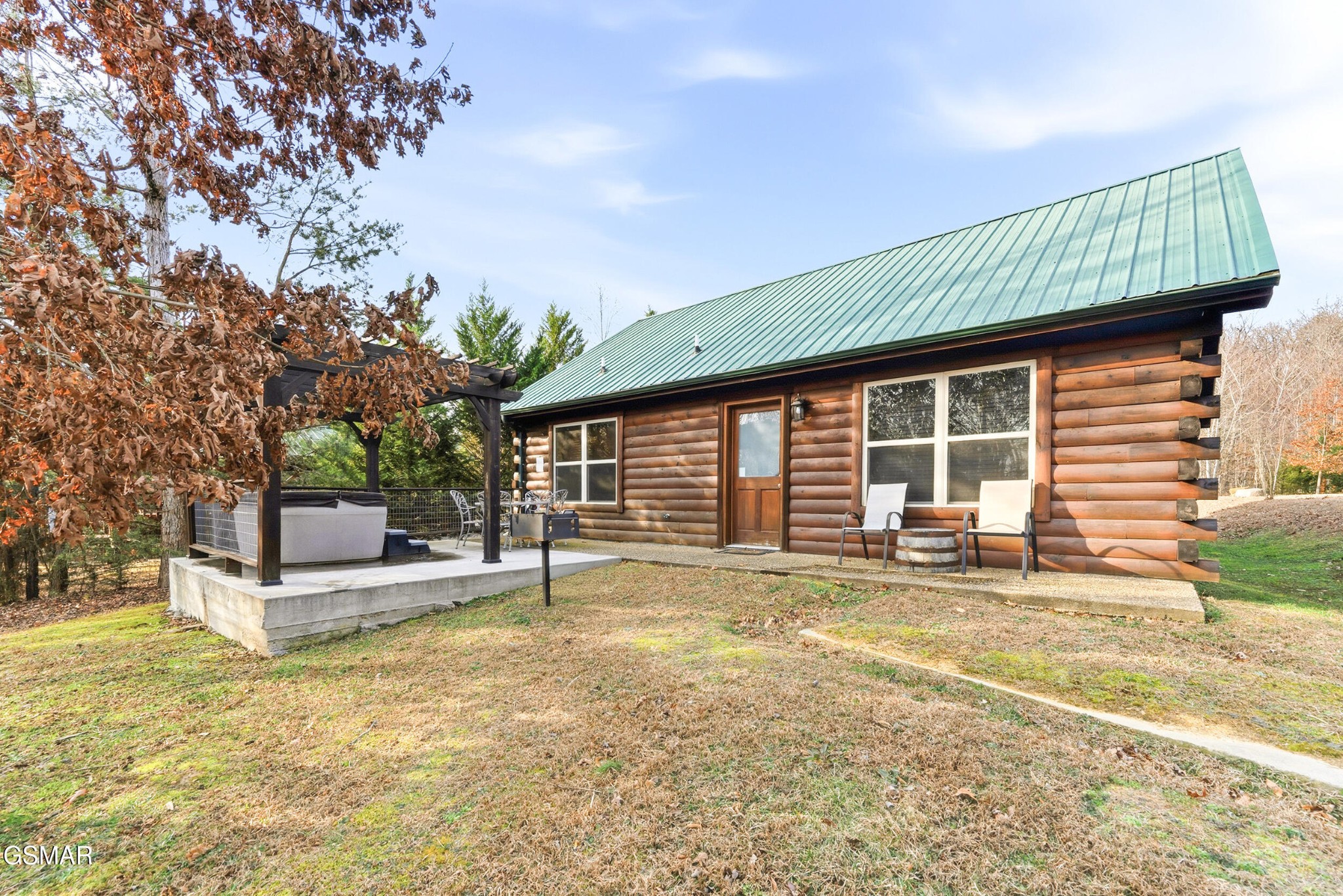 Log cabin with a green metal roof, covered hot tub patio, and chairs outside.