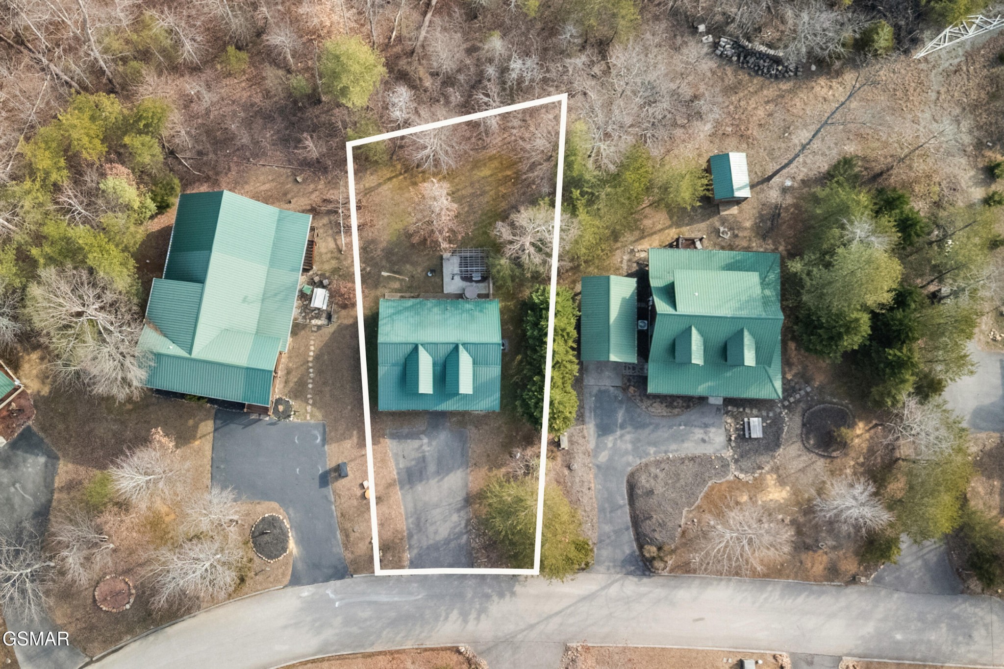 Aerial view of a green-roofed home and wooded lot outlined in white.