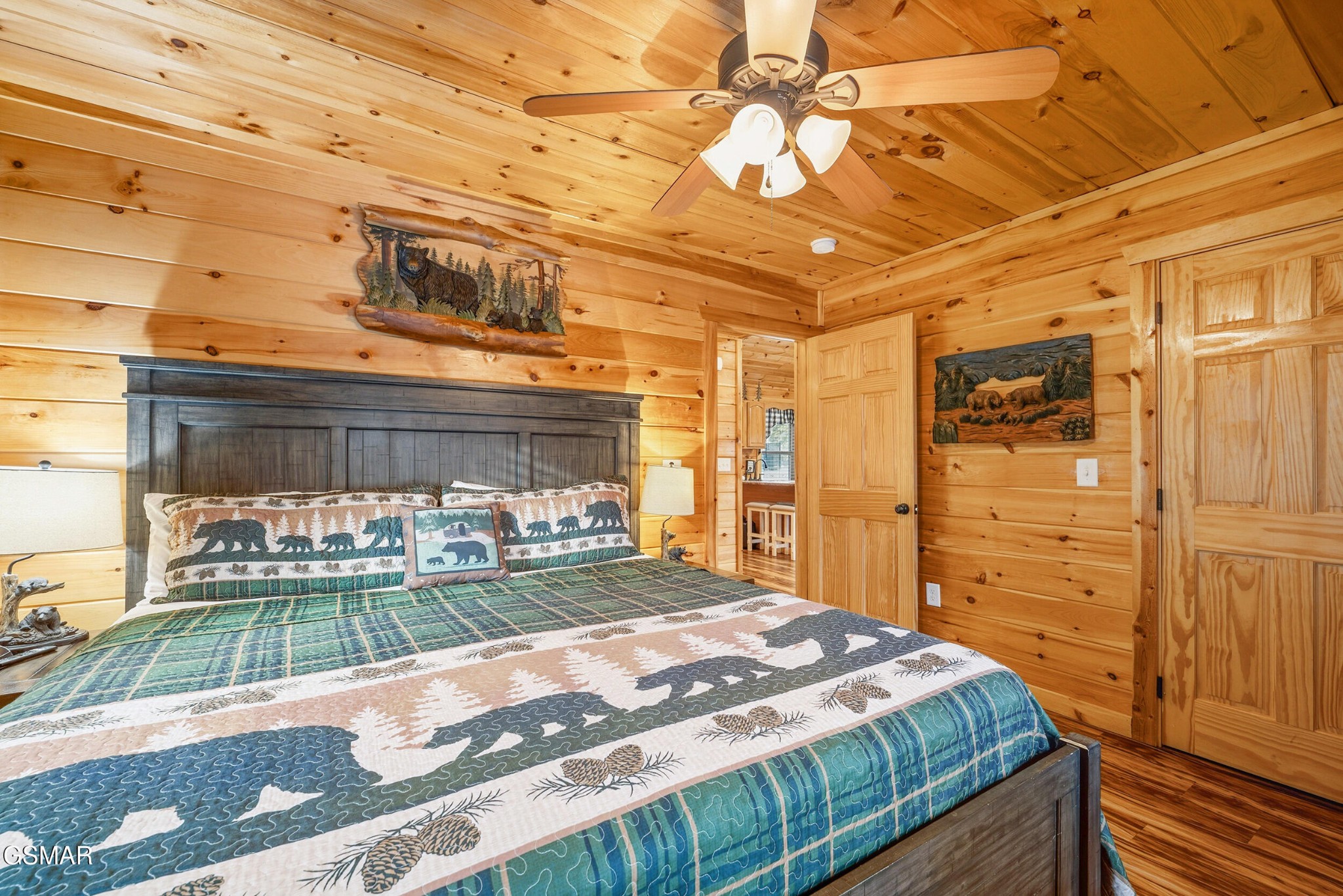 Bedroom with honey-colored log walls, a ceiling fan, and a bear-patterned quilt.