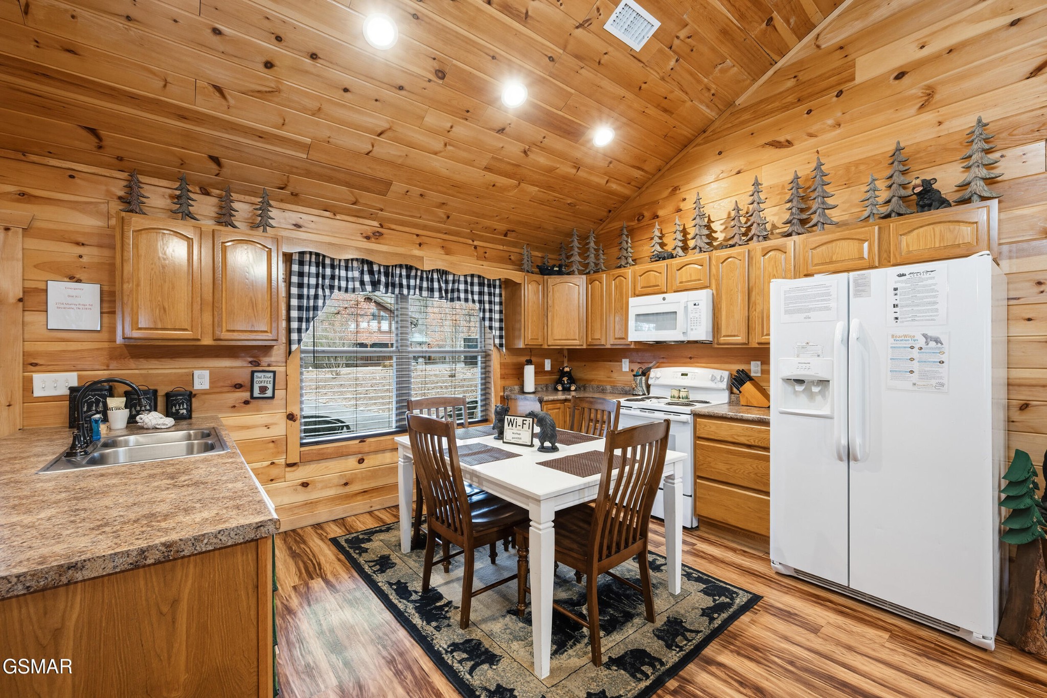 Cabin kitchen with knotty pine walls, white appliances, and a dining table beneath a vaulted ceiling.