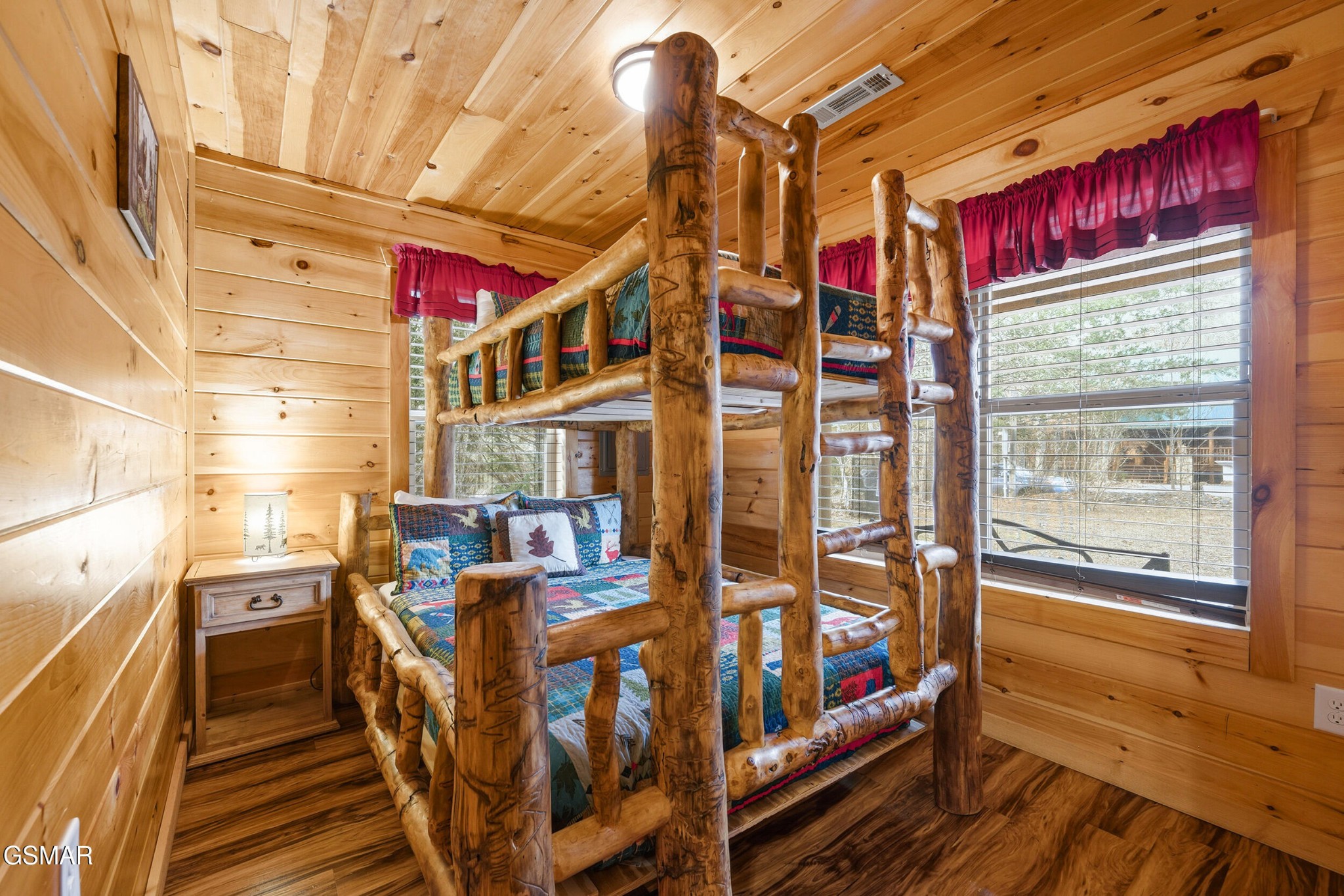 Rustic log bunk bed with colorful quilts in a wood-paneled cabin bedroom.