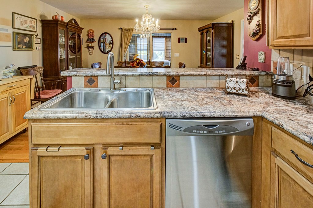 Kitchen with a double-basin sink, marbled counters, wood cabinets, and a stainless-steel dishwasher.