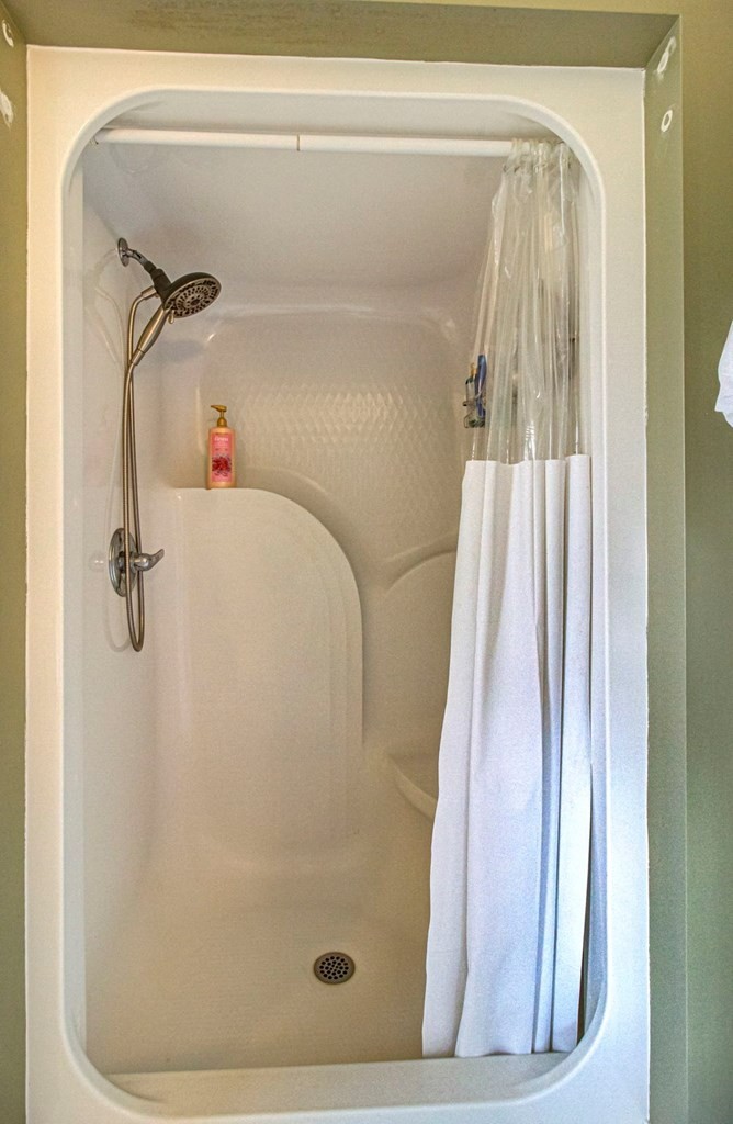 Bathroom shower stall with a bronze handheld showerhead and white curtain.