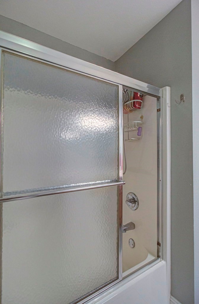 Bathroom tub and shower with frosted sliding glass doors and chrome fixtures.