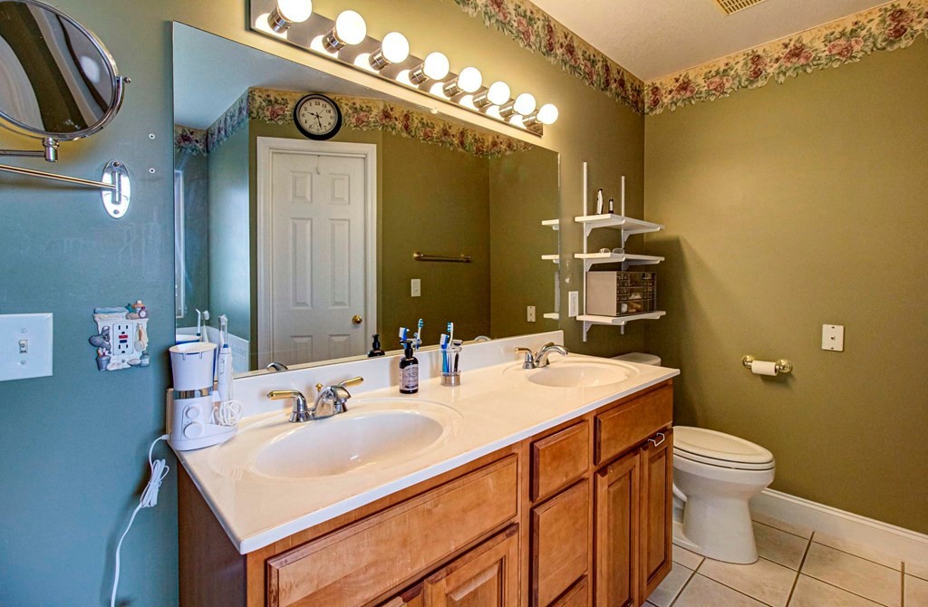 Bathroom with a double-sink vanity, illuminated mirror, wood cabinets, and floral wallpaper border.