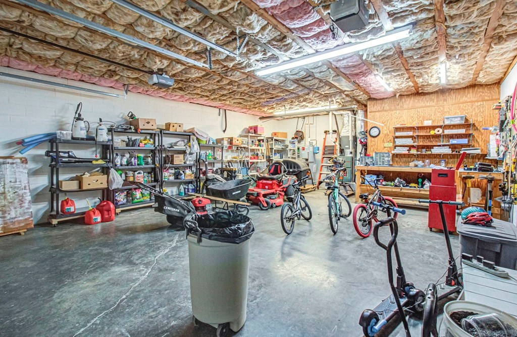 Garage workshop with exposed ceiling insulation, storage shelves, bicycles, and lawn equipment.
