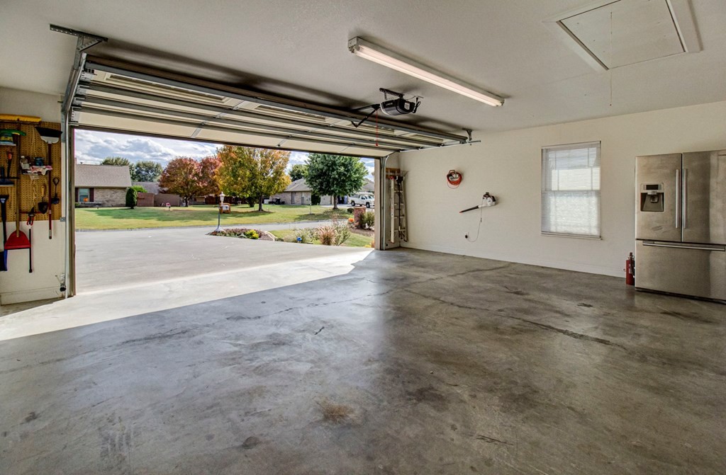 Spacious garage with a broad concrete floor, open overhead door, and stainless-steel refrigerator.