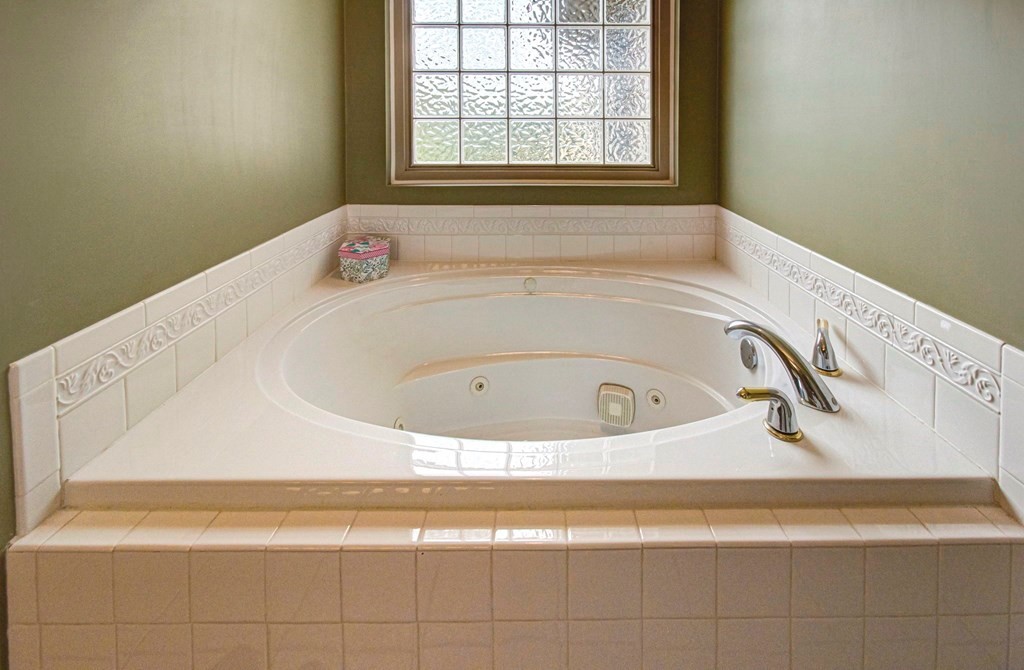 Bathroom with a white corner jetted tub beneath a textured-glass window.