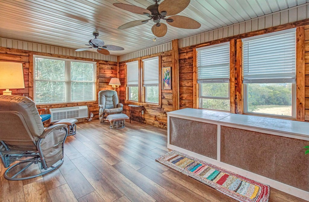 Rustic sunroom with log walls, broad windows, reclining chairs, and a long counter.