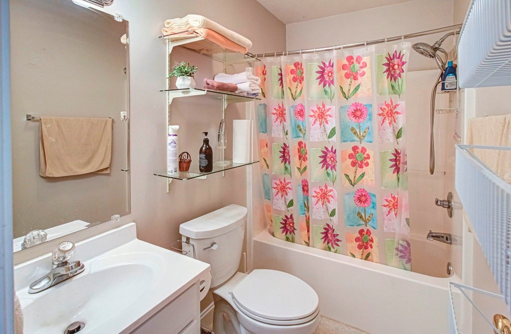 Bathroom with a white vanity and toilet beside a bathtub with a colorful floral shower curtain.