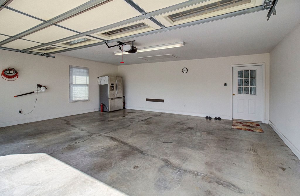 Vacant garage with a concrete floor, overhead door, refrigerator, and white side-entry door.