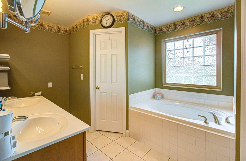 Bathroom with a corner jetted tub beneath a glass-block window and a double-sink vanity.