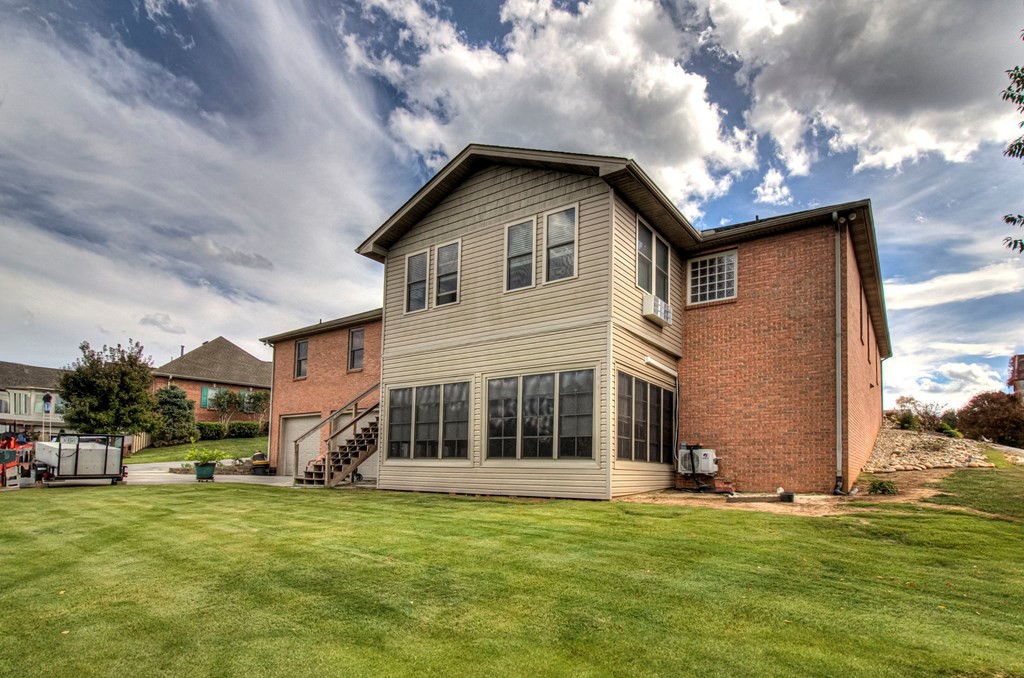 Rear exterior of a two-story home with tan siding, red brick, and a broad lawn.