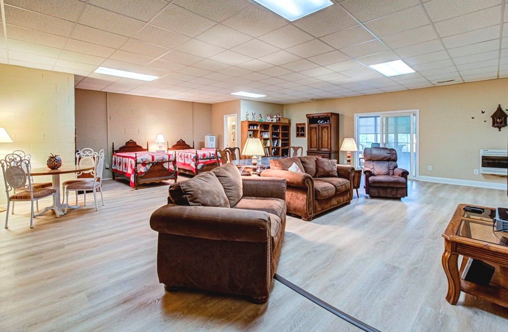Furnished open-plan room with brown sofas, two beds, a dining table, and sliding glass doors.
