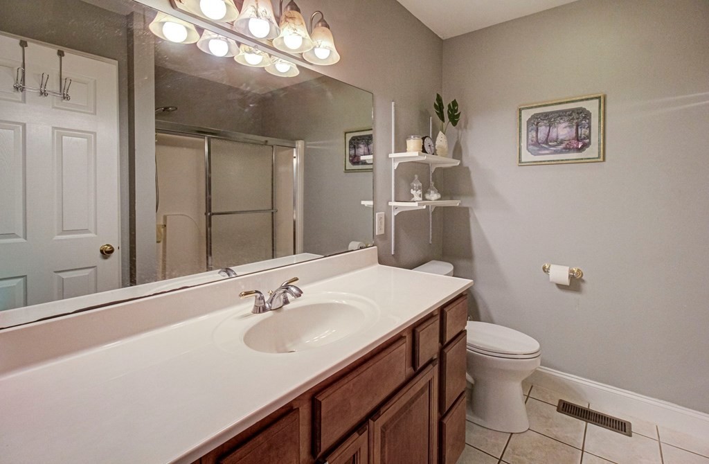 Bathroom with a wood vanity, large mirror, glass shower enclosure, and toilet.