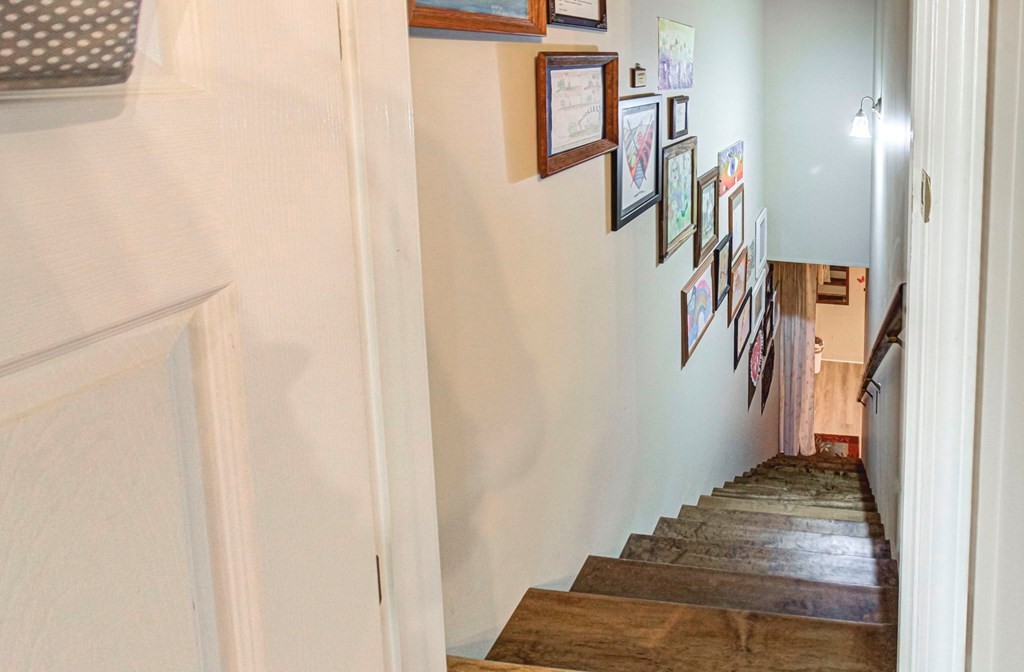 Wood-finished staircase descending past a gallery wall of framed artwork.