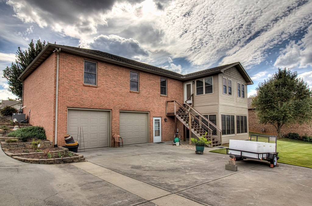 Two-story brick-and-siding home with two garage doors, a raised staircase, and a wide concrete driveway.