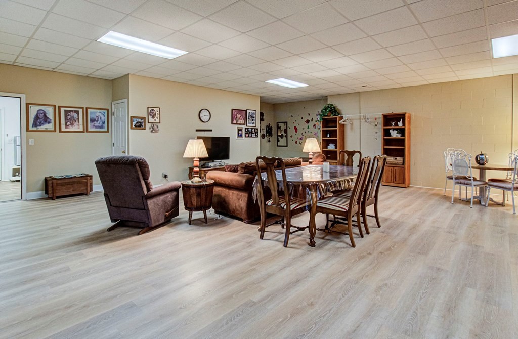 Furnished living and dining area with a long table, brown seating, and light wood-look floors.