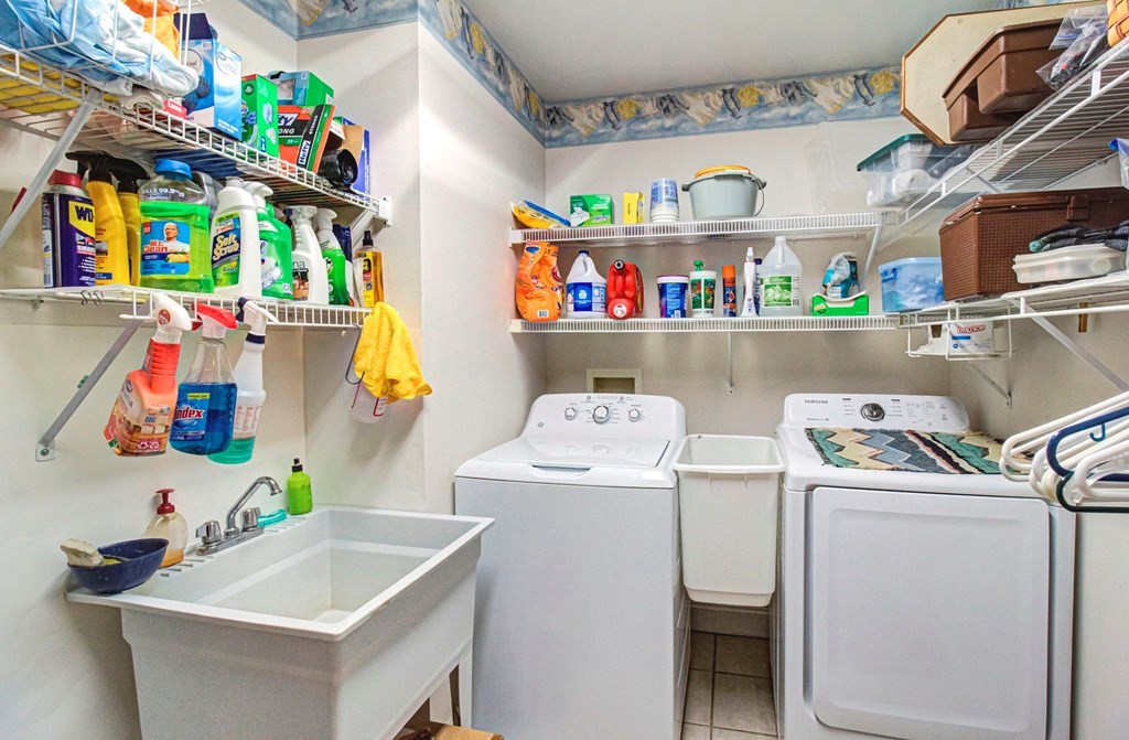 Laundry room with washer, dryer, utility sink, and wall-mounted wire shelves stocked with supplies.