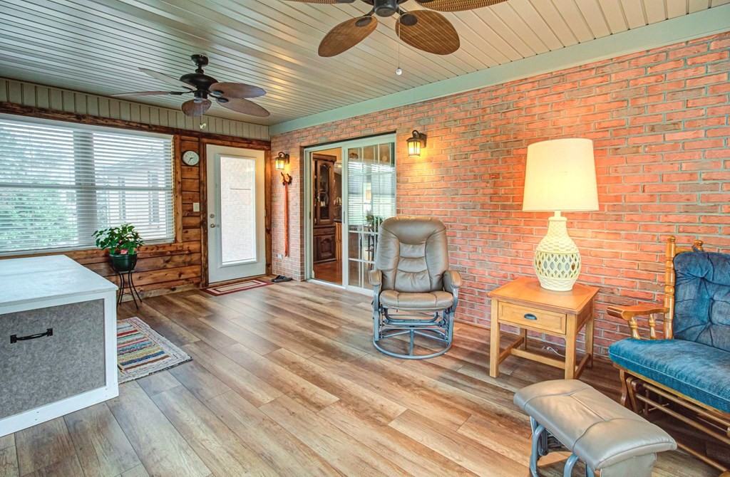 Furnished sunroom with a brick wall, two ceiling fans, and sliding glass doors.